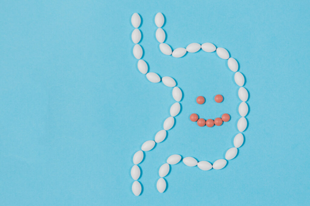 Pillen formen den Umriss eines Magens, mit einem lächelndem Smiley darin. 